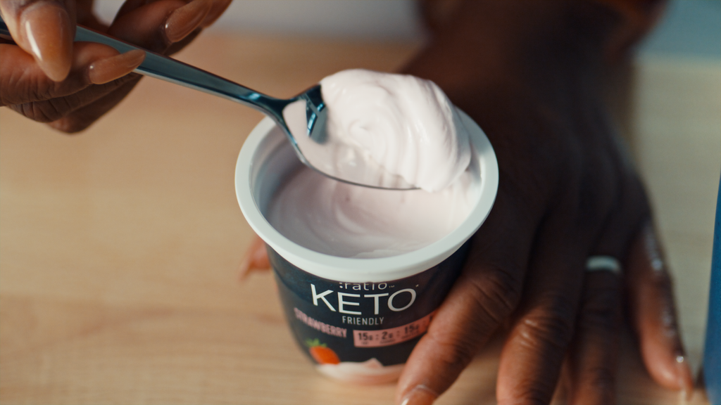 An open yogurt cup with a black spoon filled with light pink yogurt.