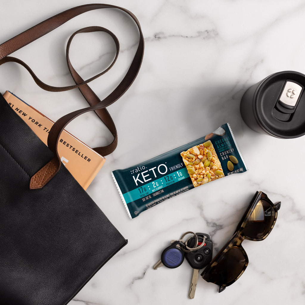 Ratio KETO Friendly Crunchy Bar and book bag with sunglasses and keys laid out on a table.