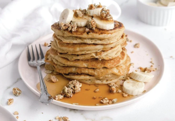 A plate of pancakes topped with bananas and ratio crunchy bars.