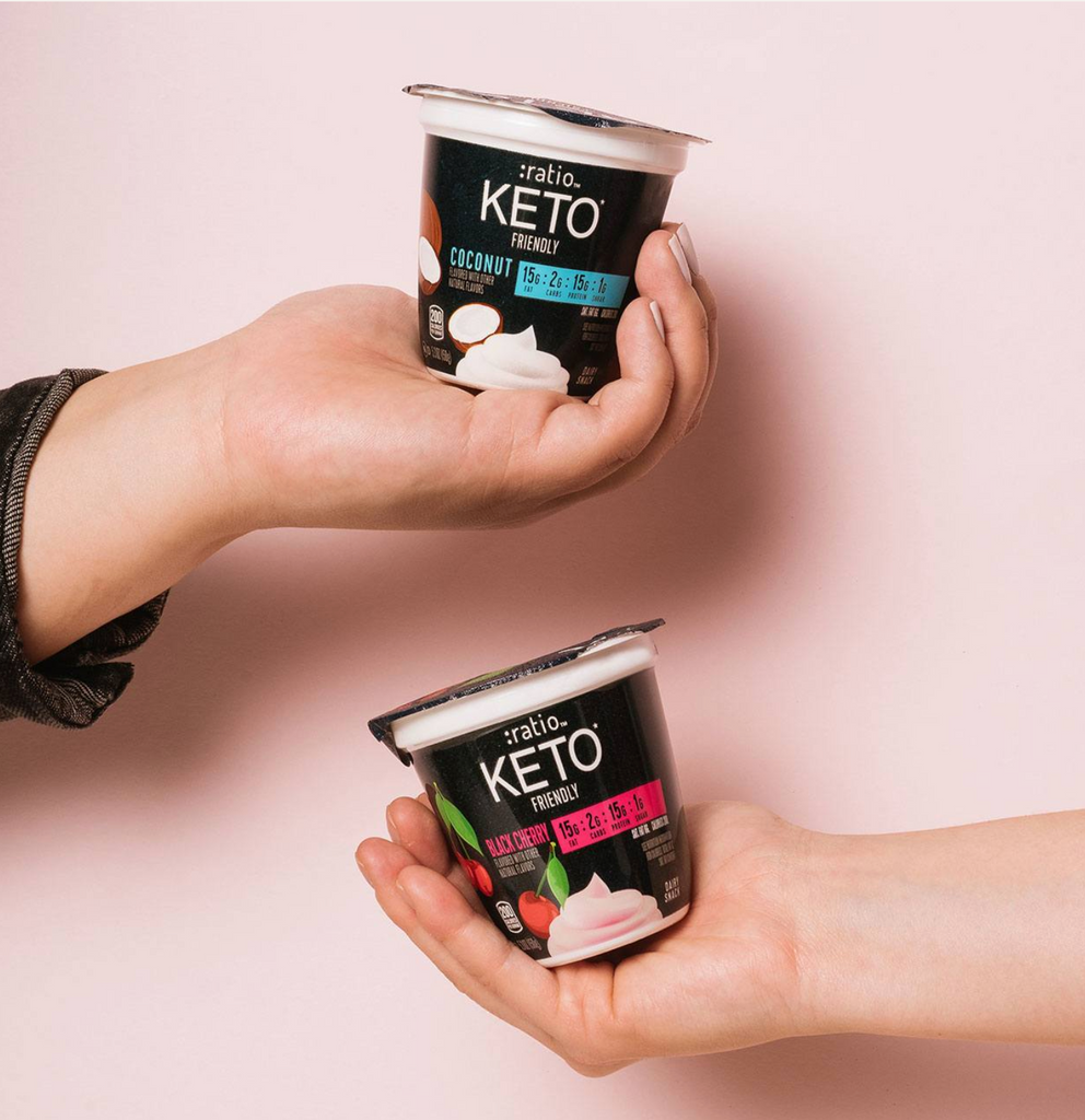 Two hands displaying coconut and black cherry-flavored Ratio KETO Friendly Yogurt Cultured Dairy Snacks.